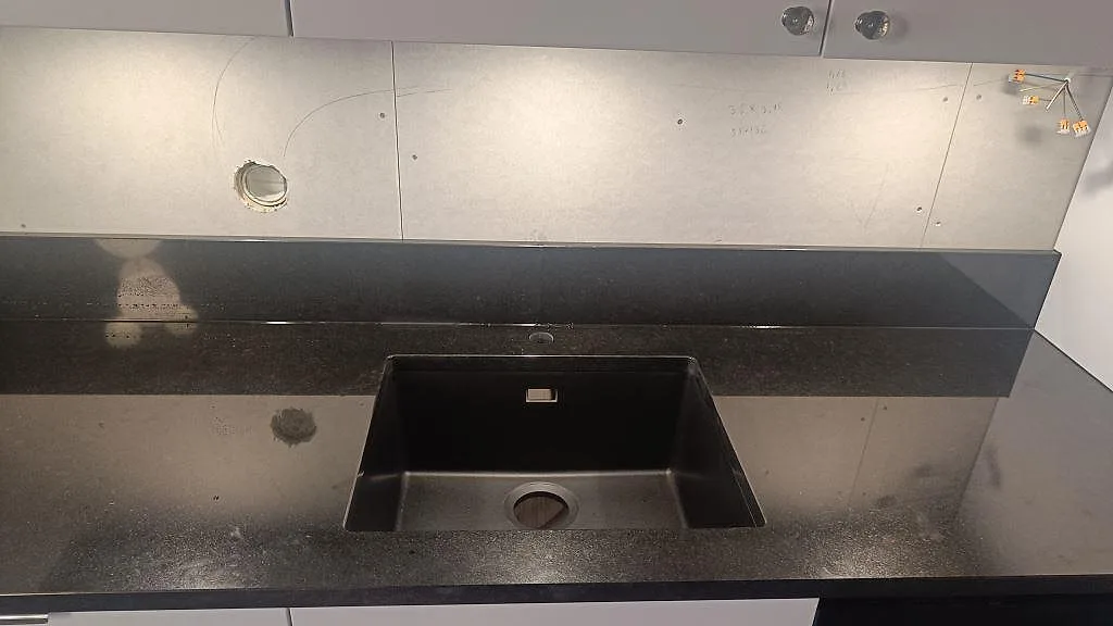 Närbild av polerad Nero Assoluto granit vid diskhozonen med mörk ho och låg stänkkant i köket i Tibro.