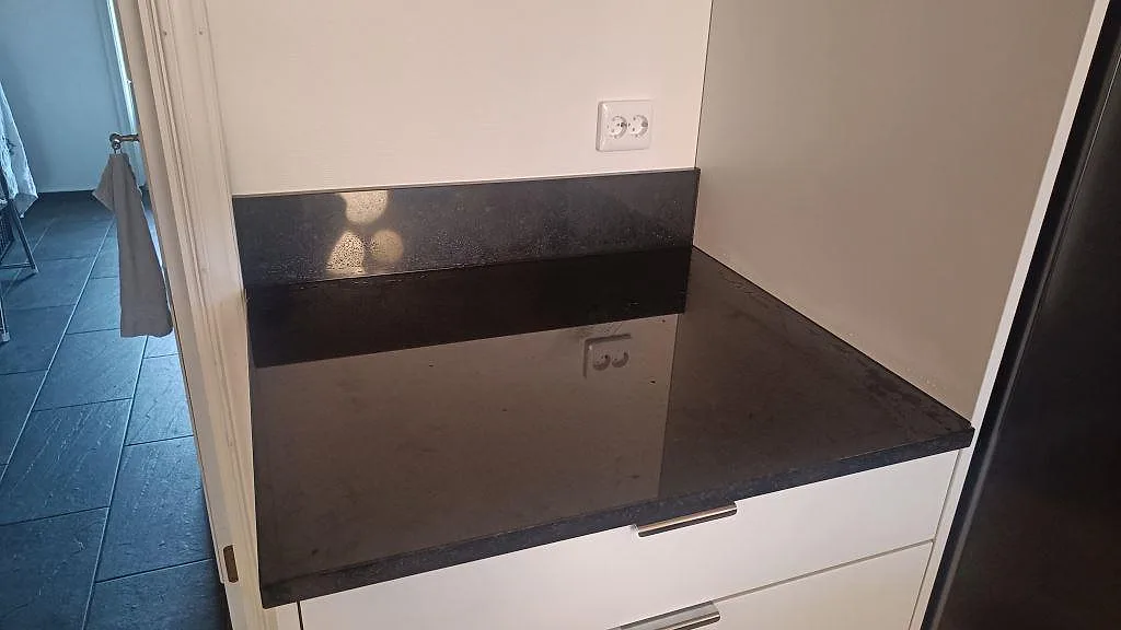 Sidobänkskiva i polerad Nero Assoluto granit med låg stänkkant och speglingar från vägguttag i Tibro.