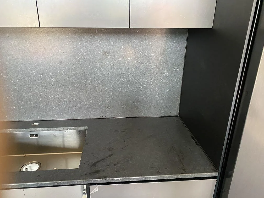 Vägghängd bänkskiva i matt Nero Assoluto med stänkskydd i samma sten och underlimmad rostfri diskho i ett kök i Töllsjö.