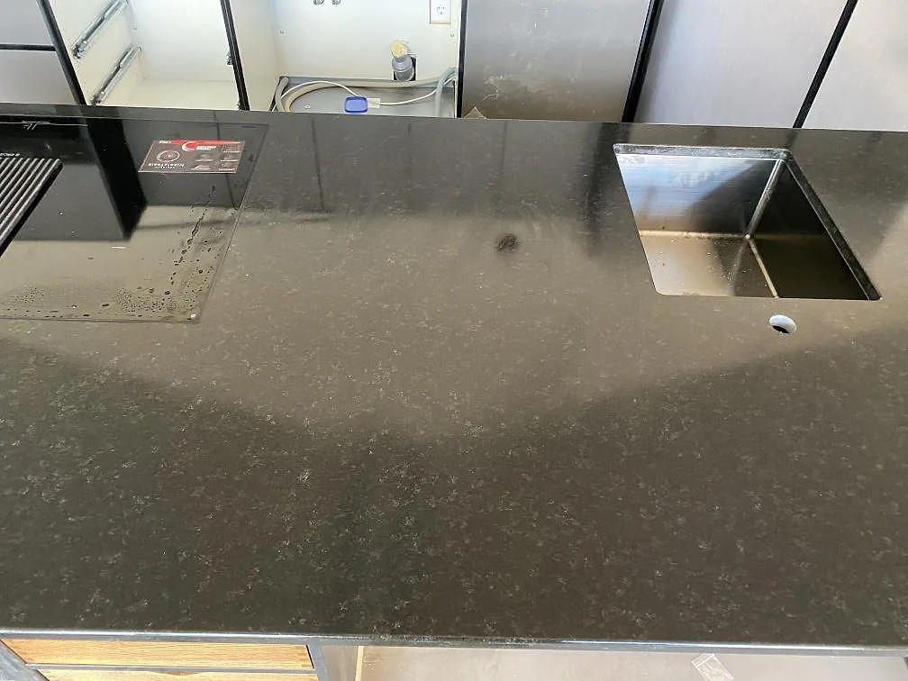 Ovanifrån av köksö i matt Nero Assoluto med urtag för induktionshäll och fyrkantig underlimmad diskho samt blandarhål i ett kök i Töllsjö.