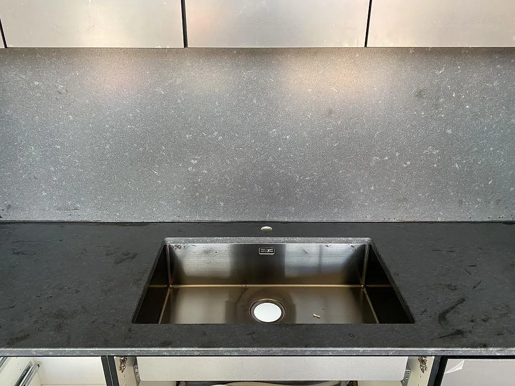 Underlimmad rostfri diskho i svart Nero Assoluto granit med matt stänkskydd och borrat blandarhål i ett kök i Töllsjö.