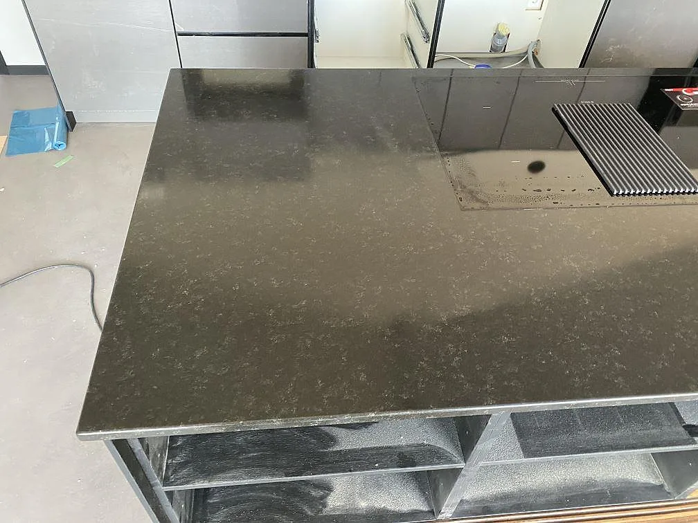 Infälld induktionshäll med neddraglucka i en köksö av svart Nero Assoluto granit med matt yta i ett kök i Töllsjö.