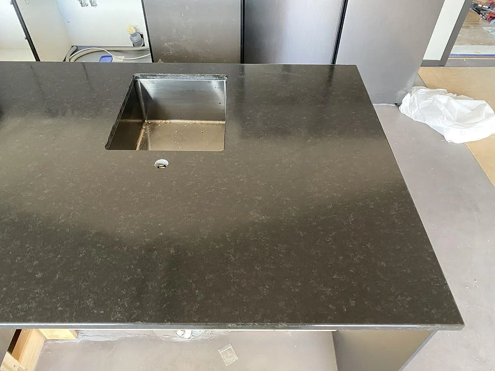 Fyrkantig underlimmad rostfri diskho i en köksö av matt Nero Assoluto granit med separat blandarhål i ett kök i Töllsjö.