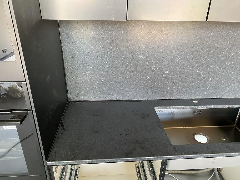 Bänkskiva i matt Nero Assoluto granit med uppvikt stänkskydd och underlimmad rostfri diskho över öppna lådskenor i ett kök i Töllsjö.
