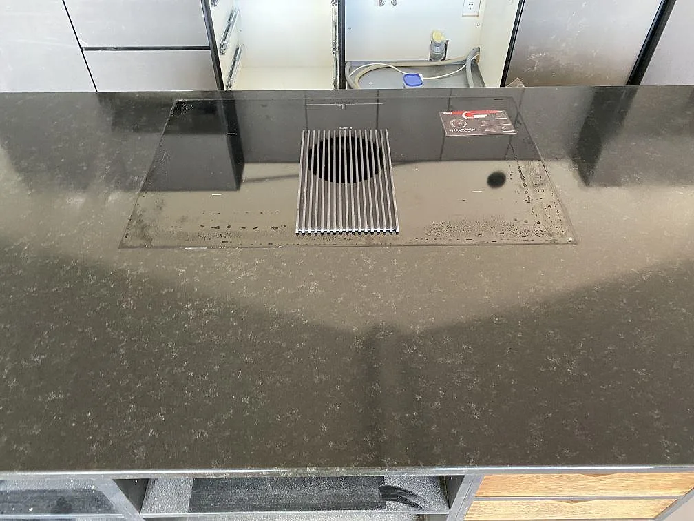 Induktionshäll infälld i nivå med en köksö av svart Nero Assoluto granit med matt yta i ett kök i Töllsjö.