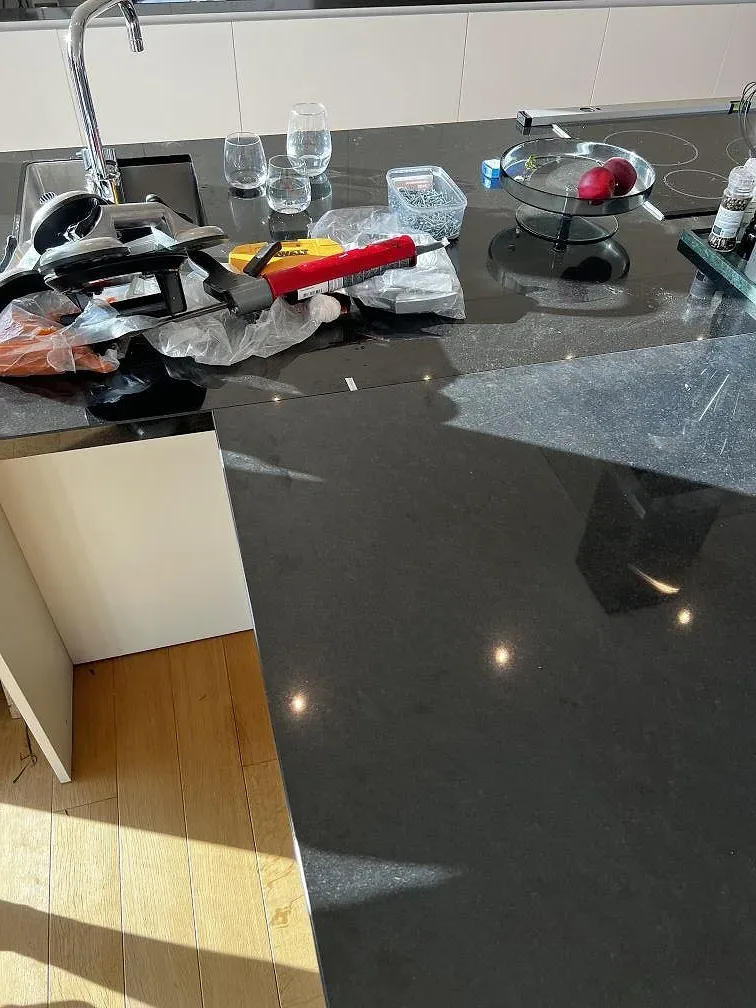 Polerad Nero Assoluto granit vid köksö och bakre bänkrad med blandare och häll i ett kök i Torslanda.