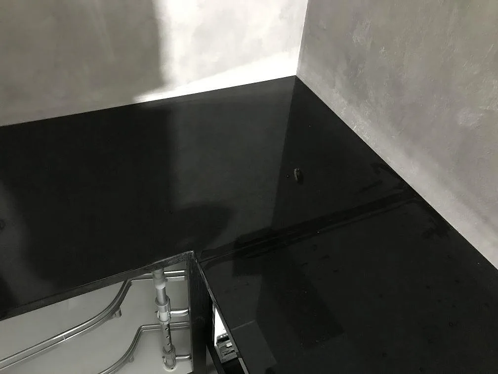 Hörnsektion med blank köksbänkskiva i Nero Assoluto granit mot ljusa väggar under montering i Torsö.