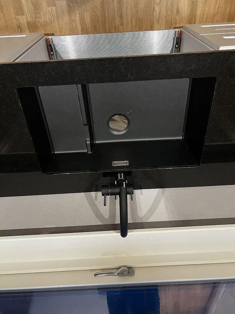 Närbild på underlimmad svart kompositdiskho och svart blandare i polerad Nero Assoluto granit i ett kök i Träslövsläge.