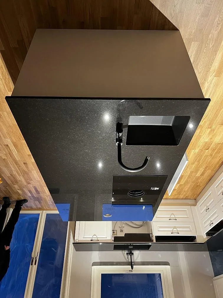 Köksö i polerad svart Nero Assoluto granit med infälld häll och underlimmad diskho mot träpanel i ett kök i Träslövsläge.