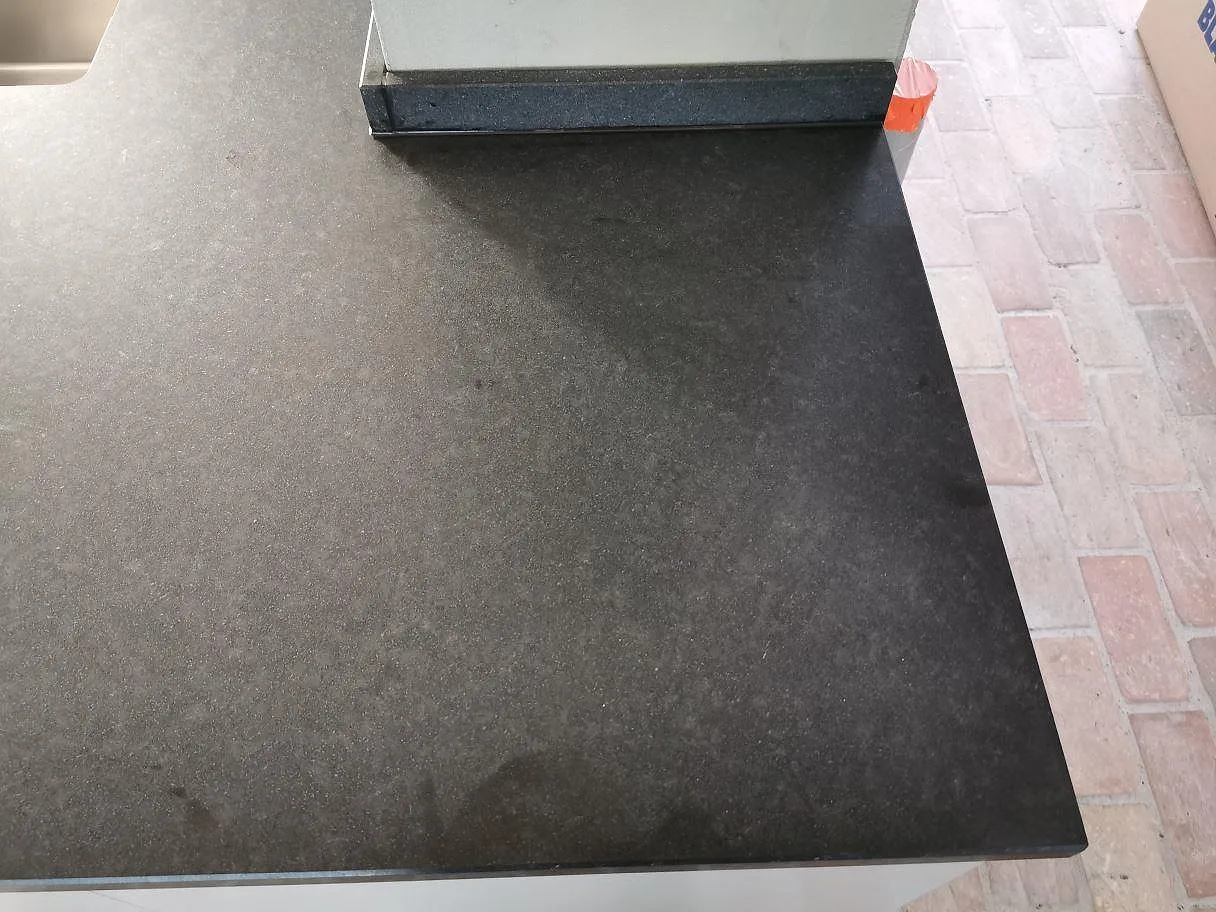 Hörn av matt svart Nero Assoluto granitbänkskiva med rakfasad kant ovanför tegelgolv i ett kök i Trelleborg.