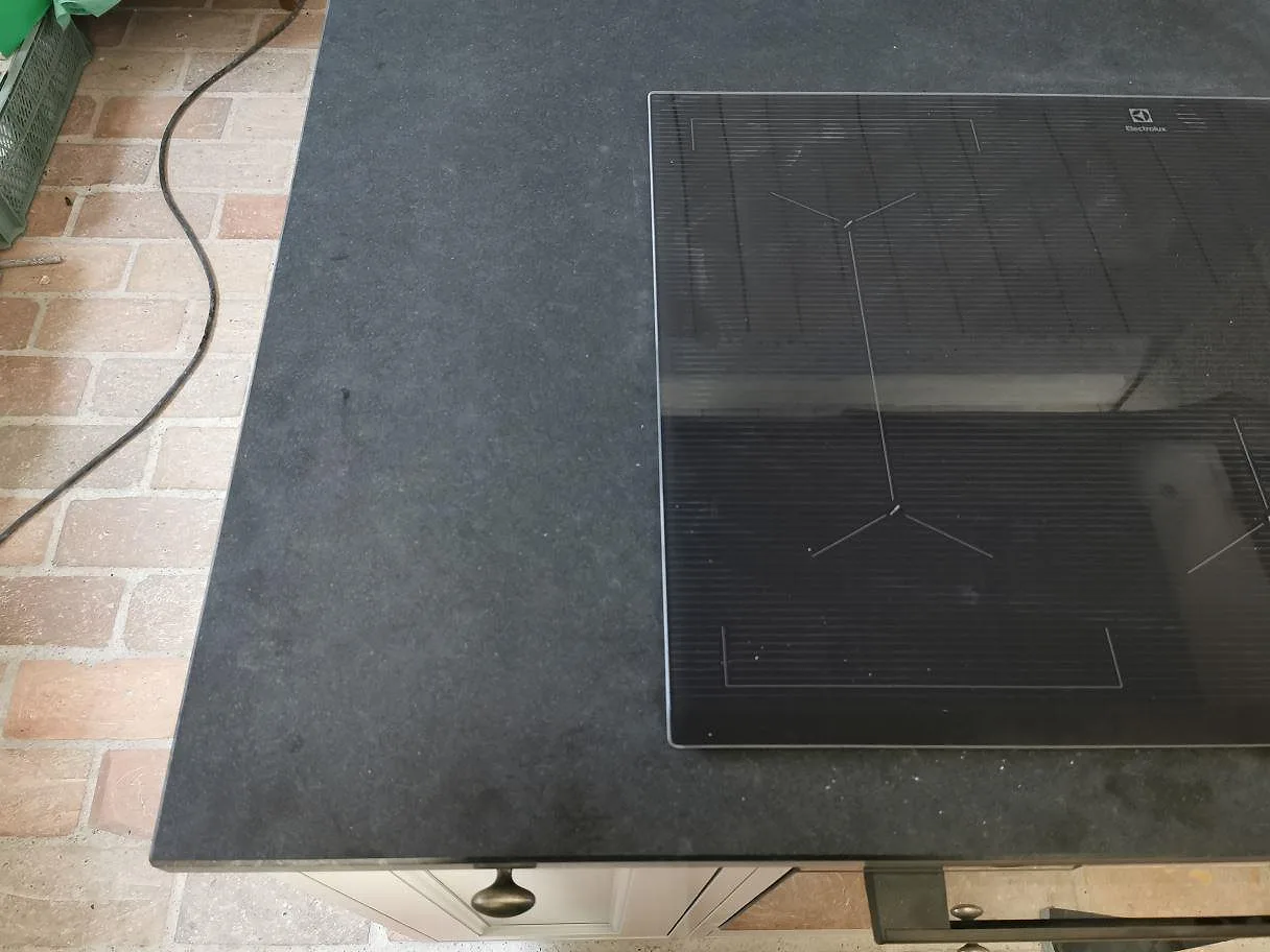 Köksbänk i matt svart Nero Assoluto granit med övermonterad Electrolux induktionshäll och ljusa köksluckor i ett kök i Trelleborg.