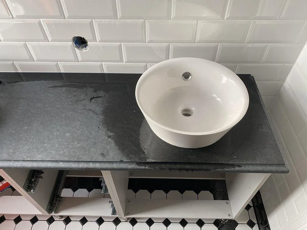 Detalj av matt Nero Assoluto granit som badrumsskiva med ett ovanpåliggande vitt tvättställ i trelleborg.