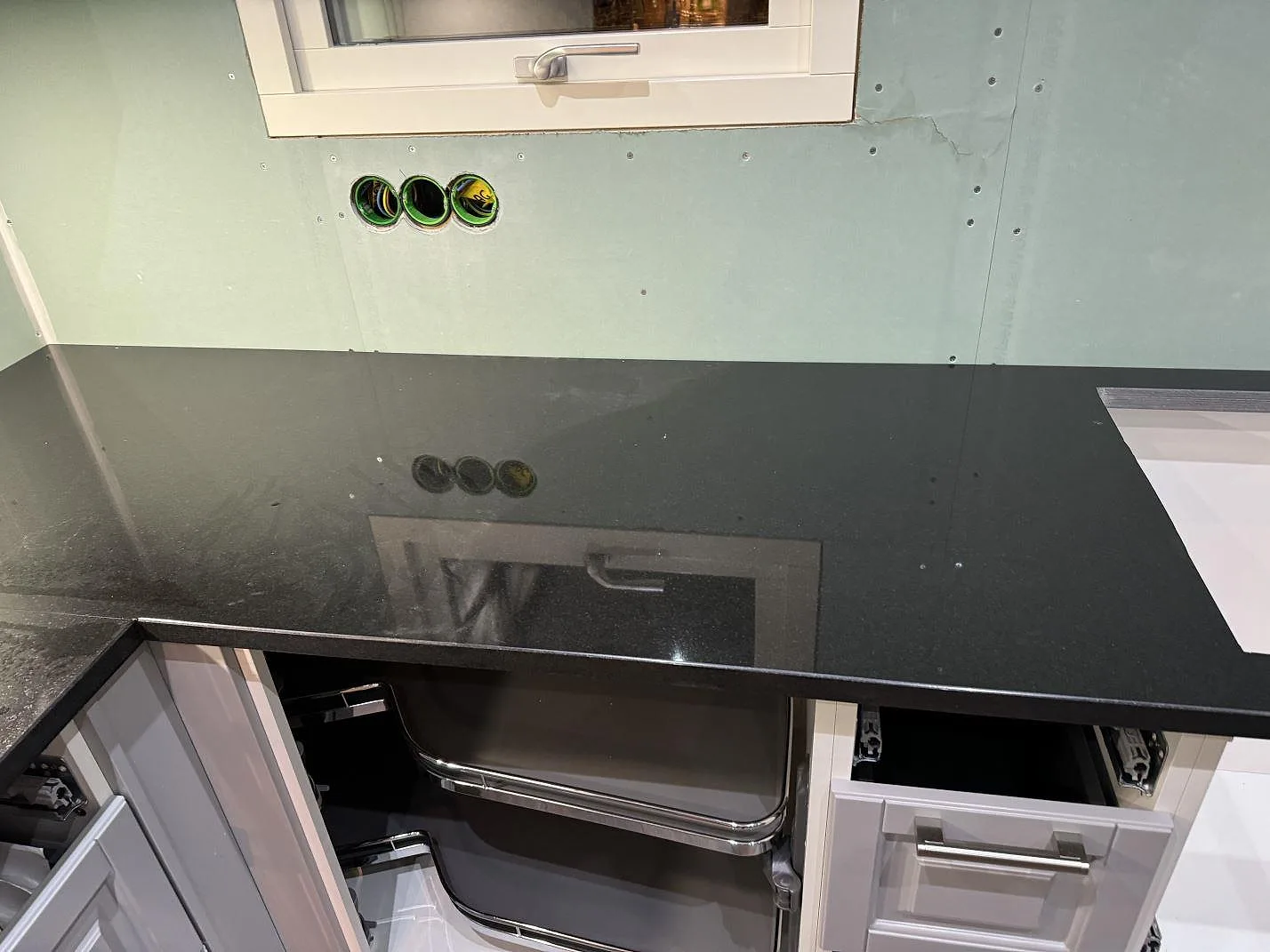 Rak köksbänk i polerad Nero Assoluto granit under fönster, med öppen stomme och blank svart yta i Trollhättan.