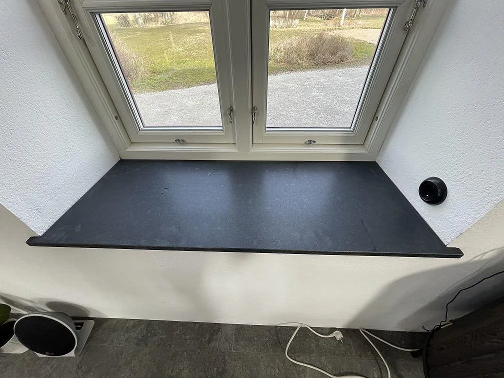 Bred fönsterbänk i svart Nero Assoluto-granit med matt yta monterad under ett fönster i Tygelsjö.
