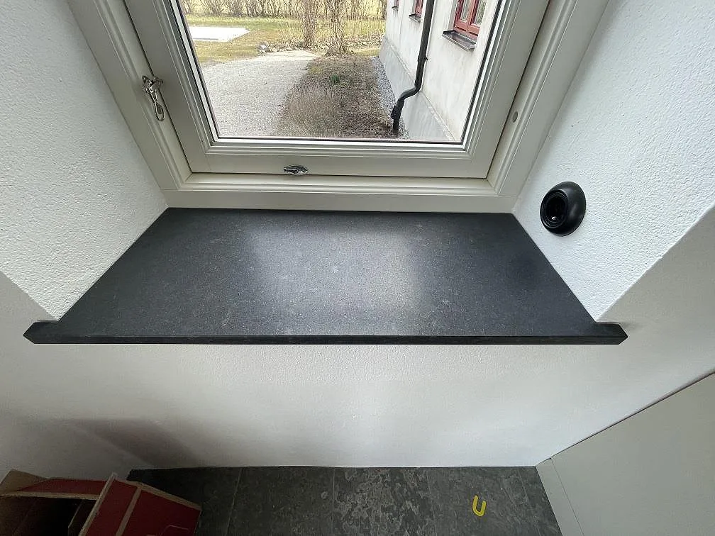 Fönsterbänk i Nero Assoluto-granit i en fönsternisch med vita väggar, svart matt sten, i Tygelsjö.