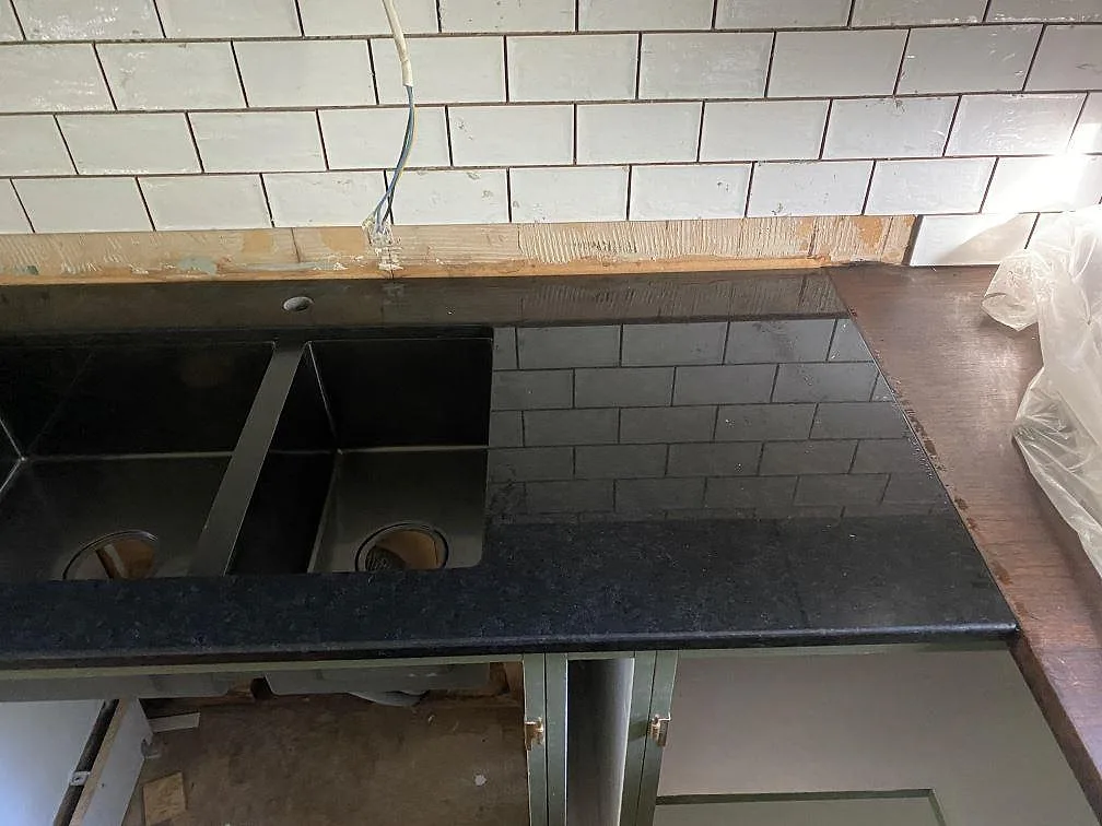 Eldriven bänkskiva i polerad svart granit Nero Assoluto med två underlimmade diskhoar och borrat blandarhål i ett kök i Ulricehamn.