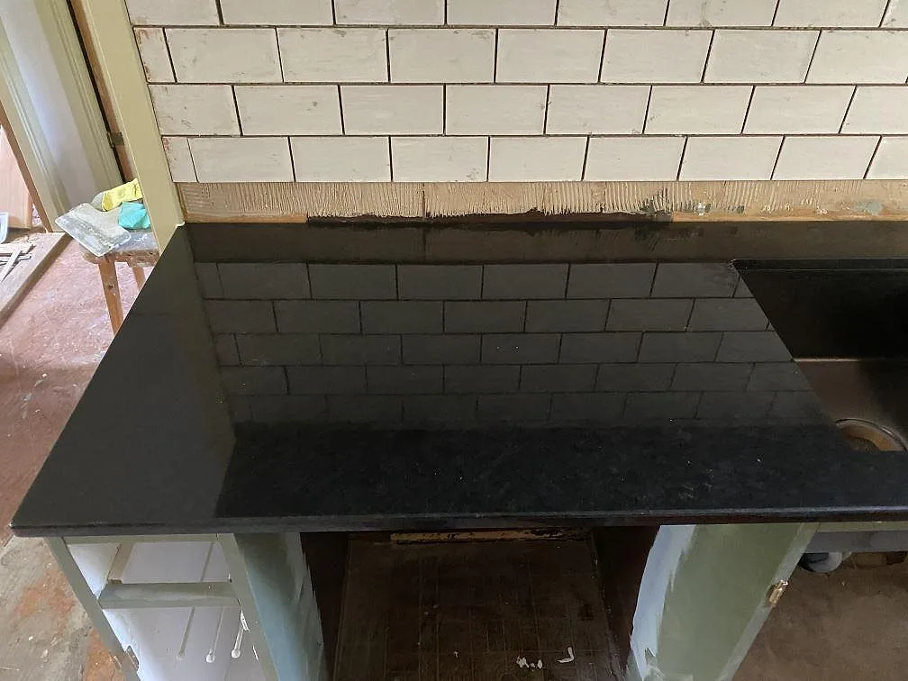 Köksbänkskiva i polerad Nero Assoluto, svart granit, med spegelblank yta som reflekterar det vita kaklet i ett kök under montering i Ulricehamn.