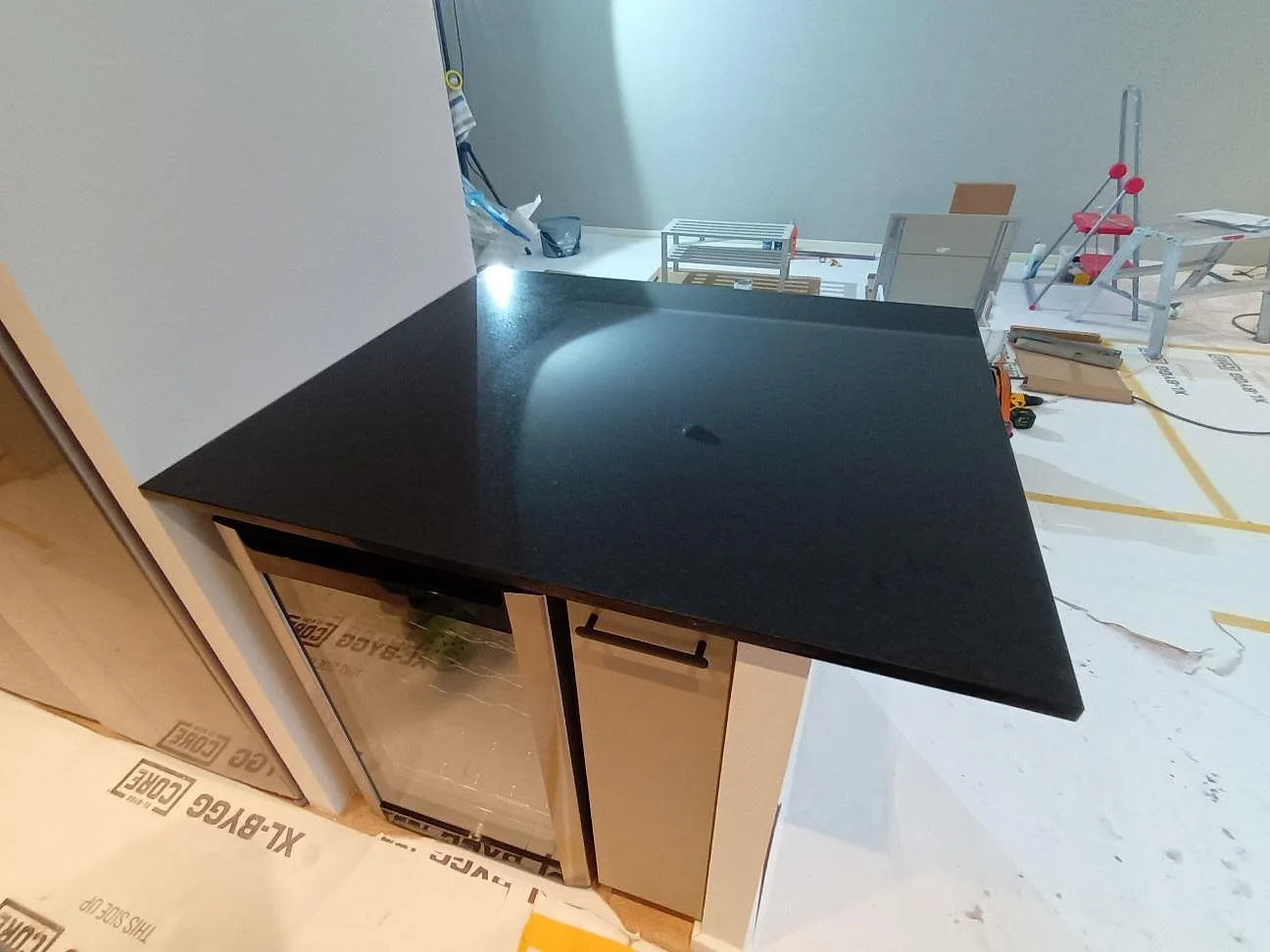 Närbild på polerad Nero Assoluto granit som installerad köksbänkskiva över ljusa köksstommar i Vällingby.