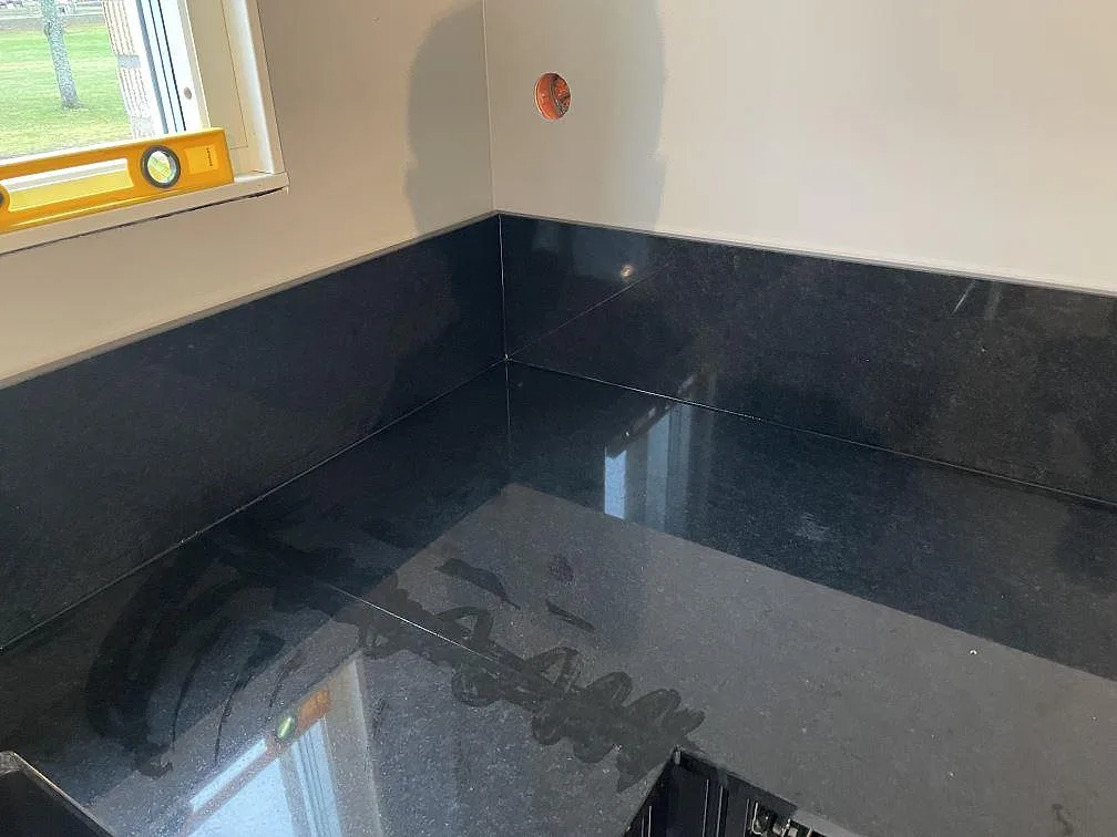 Närbild på hörn och stänkskydd i polerad Nero Assoluto granit i ett kök i Väring.