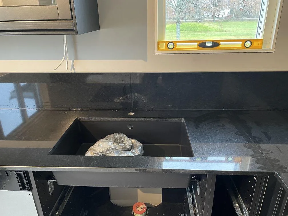 Polerad köksbänkskiva i Nero Assoluto granit med synlig diskhodel och stänkskydd i Väring.