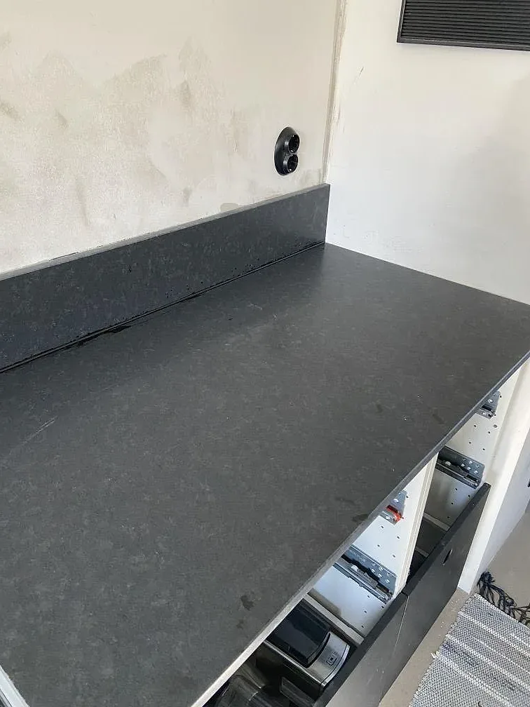 Köksbänkskiva i matt svart Nero Assoluto-granit med uppvikt stänkkant, monterad i ett kök under installation i Västra Frölunda.