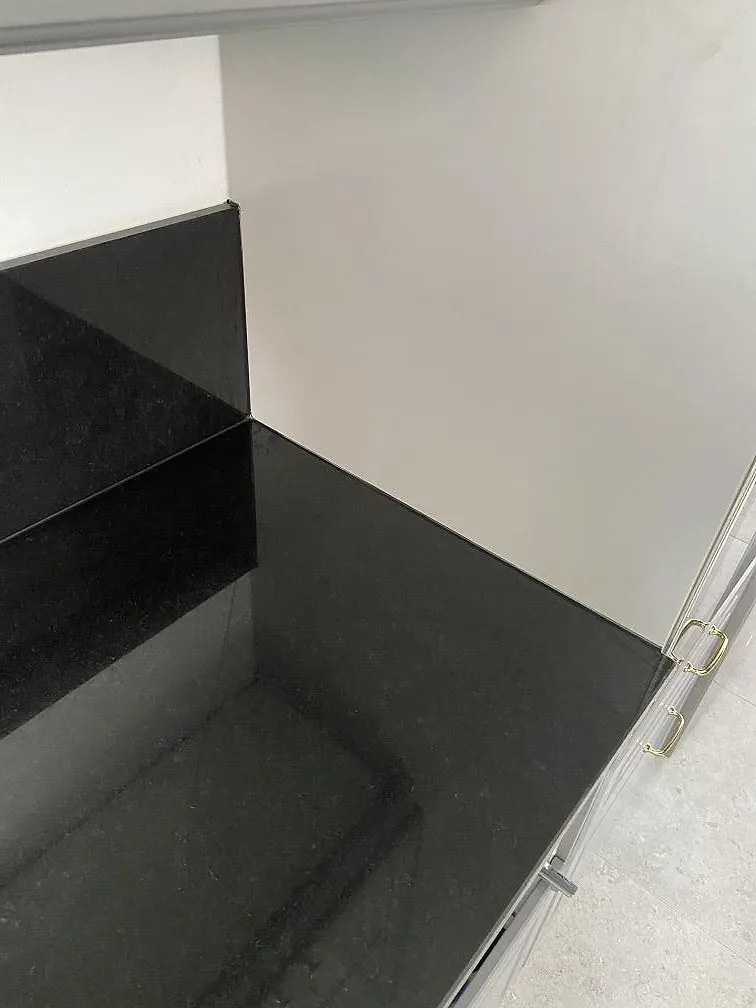 Hörn av polerad Nero Assoluto-granitbänkskiva med blank spegelyta mot vit vägg i ett kök i Västra Frölunda.