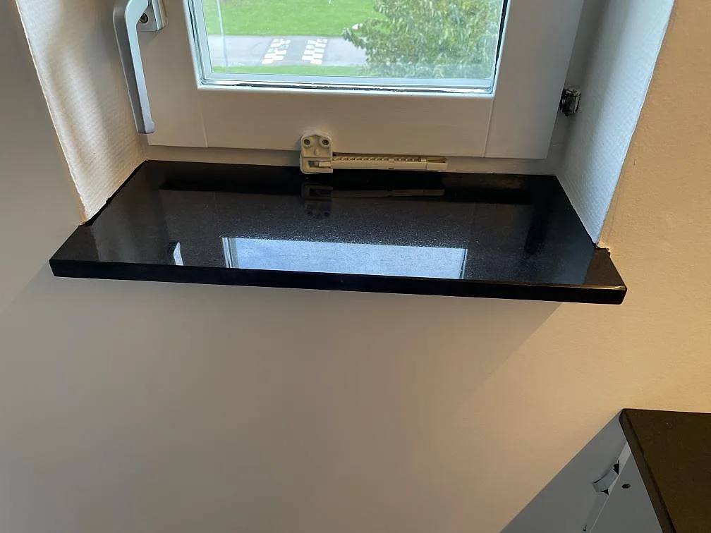 Svart fönsterbänk i polerad Nero Assoluto granit med spegling från fönstret i Vellinge.