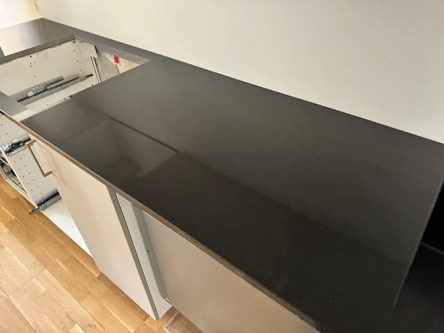 Lång köksbänkskiva i svart polerad Nero Assoluto granit på vita köksstommar och trägolv i Vellinge.
