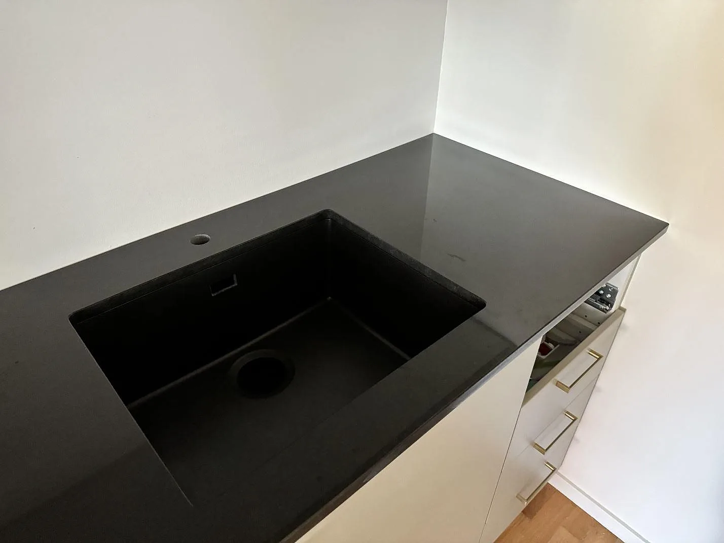 Polerad köksbänkskiva i Nero Assoluto med svart underlimmad diskho i ett kök med vita skåp i Vellinge.