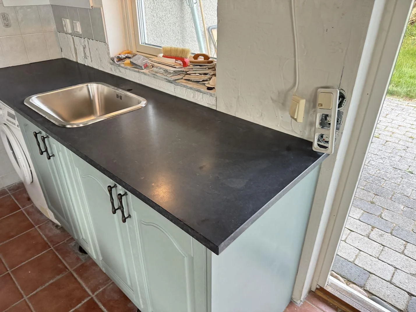 Matt köksbänkskiva i Nero Assoluto granit med rostfri diskho och mörk arbetsyta i ett kök i Viken under montering.