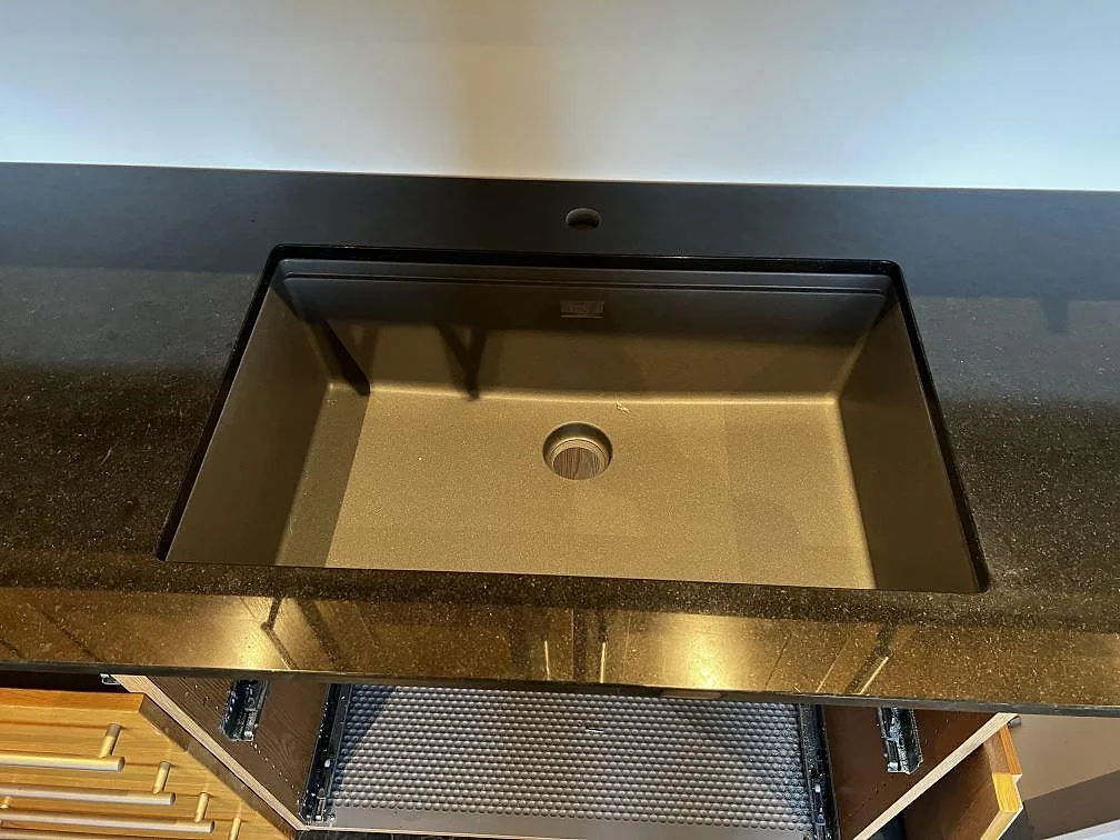 Underlimmad rostfri diskho i polerad Nero Assoluto granit med svart stänkkant och träinredning i ett kök i Ystad.