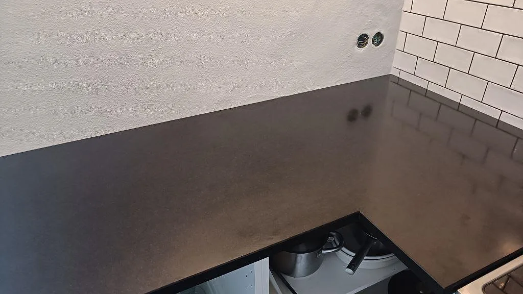 Matt köksbänkskiva i Nero Assoluto granit med mörk stenyta och väggkakel vid spisen i Ystad.