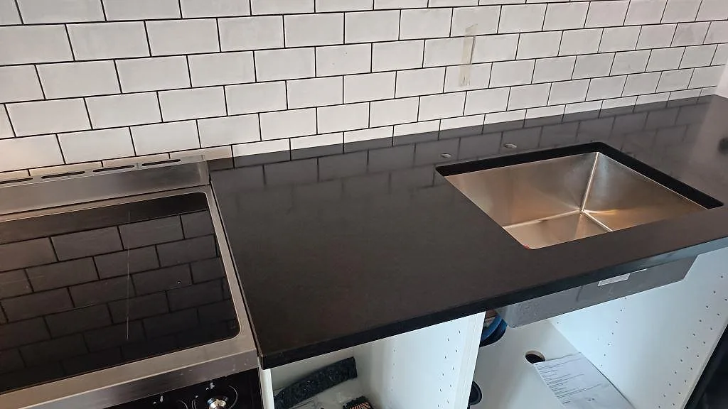 Köksbänkskiva i matt Nero Assoluto granit med rostfri diskho och fristående spis i Ystad.