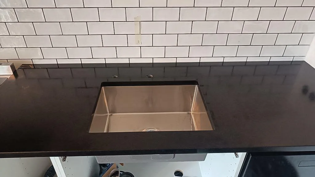 Rostfri diskho i matt Nero Assoluto granitbänkskiva framför vitt kakel i kök i Ystad.