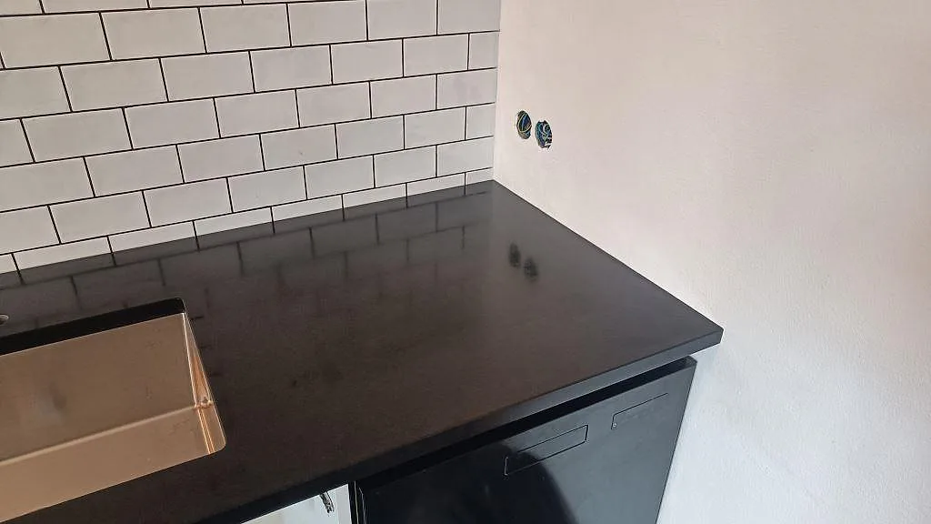 Höger del av köksbänkskiva i matt Nero Assoluto granit med rostfri diskho och svart vitvara i Ystad.