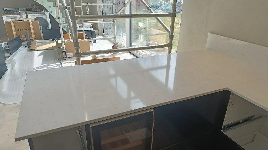 Polerad köksbänkskiva i vit Technistone Noble Areti Bianco vid ett stort fönster i ett kök under montering i Torslanda.