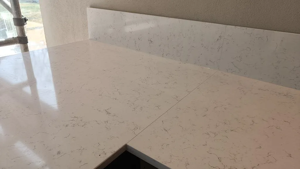 Närbild på polerad vit Technistone Noble Areti Bianco med grå ådring och heltäckande stänkvägg i ett kök i Torslanda.