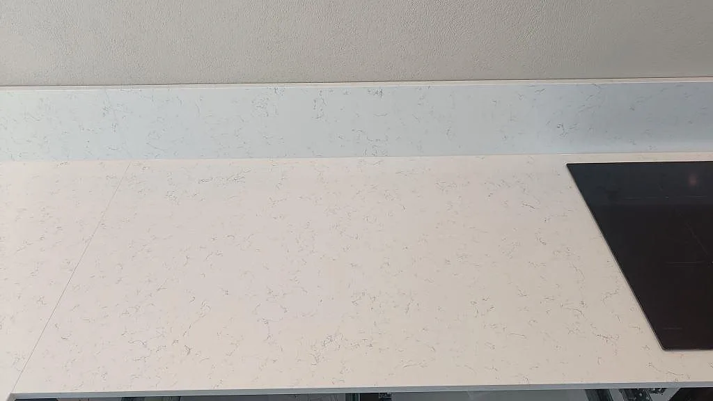 Topbild på polerad vit Technistone Noble Areti Bianco köksbänkskiva med induktionshäll i ett kök i Torslanda.