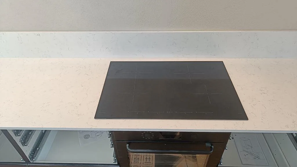 Infälld induktionshäll i polerad vit Technistone Noble Areti Bianco med heltäckande stänkvägg i ett kök i Torslanda.
