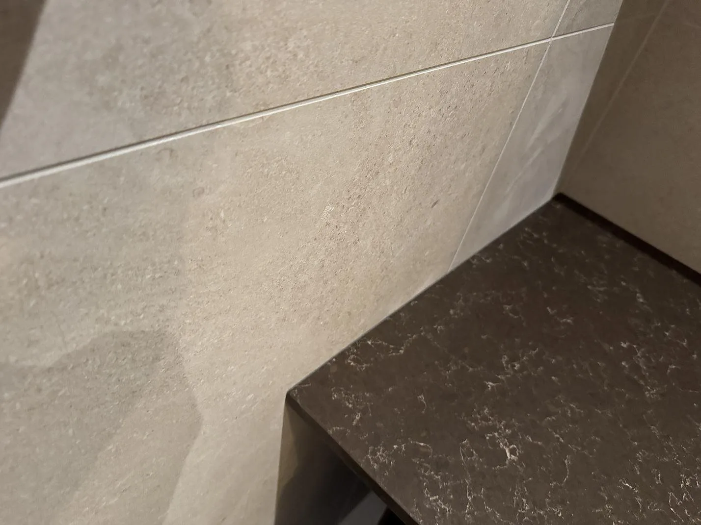 Detalj av hörnmonterad bänkskiva i Noble Athos Brown, polerad kvartskomposit, mot kaklad vägg i Malmö.