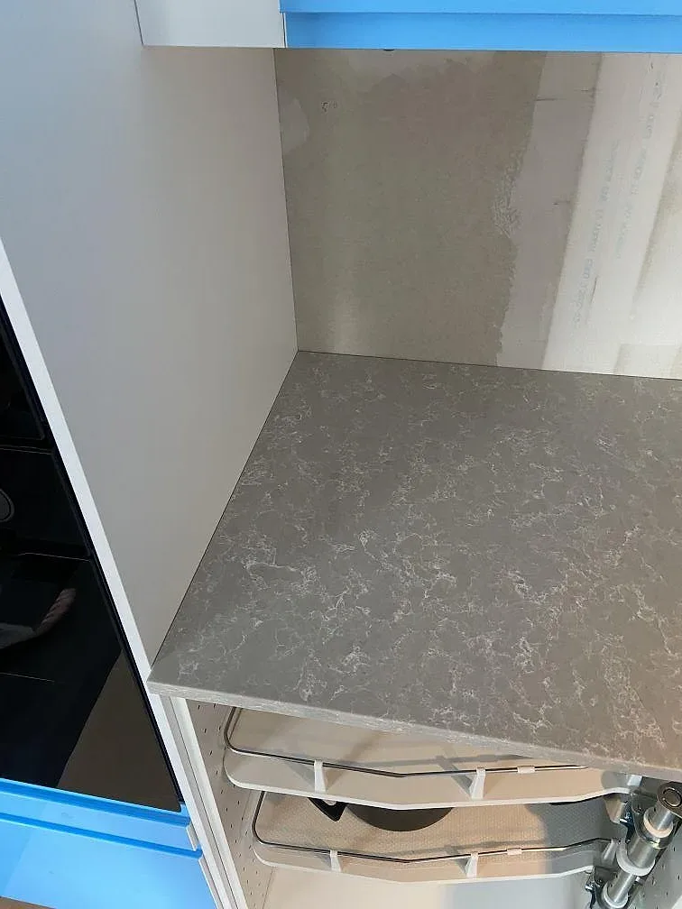 Grå kvartskomposit Noble Olympos Mist med uppvikt stänkkant i hörnet mot en köksstomme under installation i Svedala.