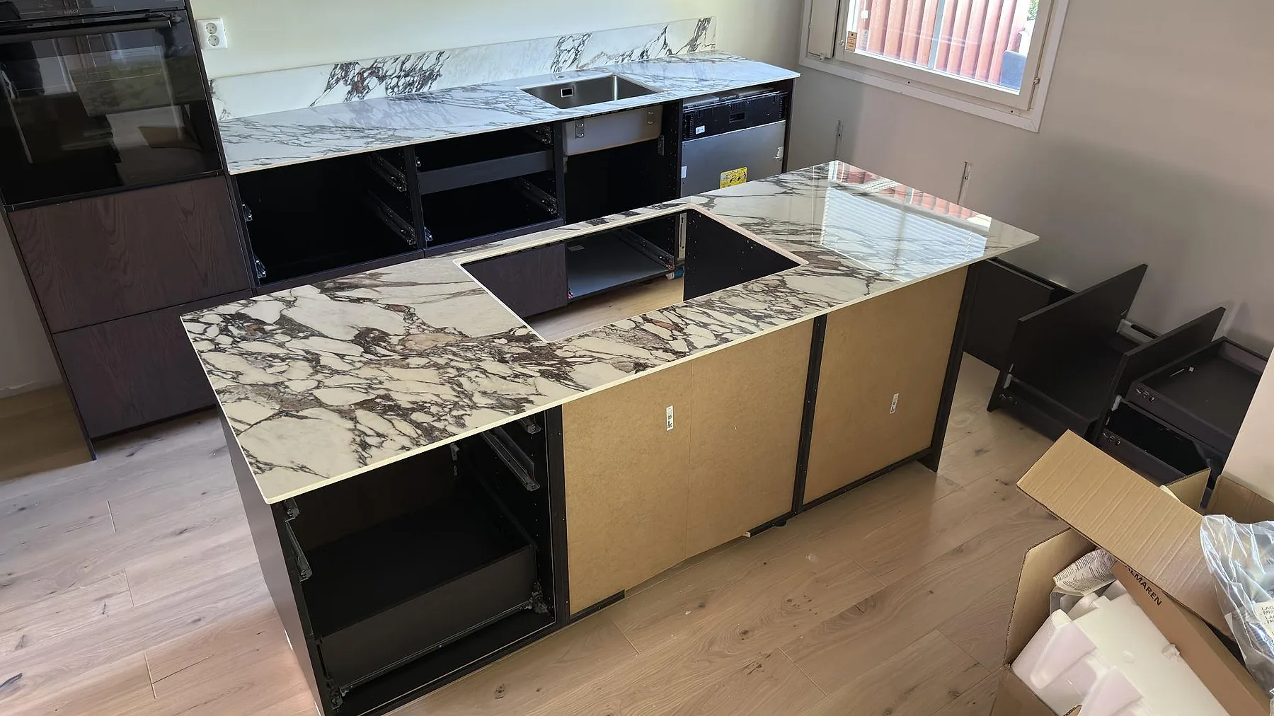Köksö i polerad keramik Nuovo Corso Arabescato Viola sedd uppifrån, med tydlig violett och grå ådring och bakre bänk med diskho i ett kök i Vällingby.