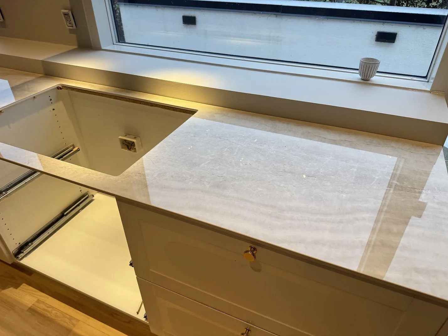 Lång polerad bänkrad i krämvit keramik Nuovo Corso Taj Mahal längs fönstret med mjuk ådring i ett kök under montering i Aalborg.