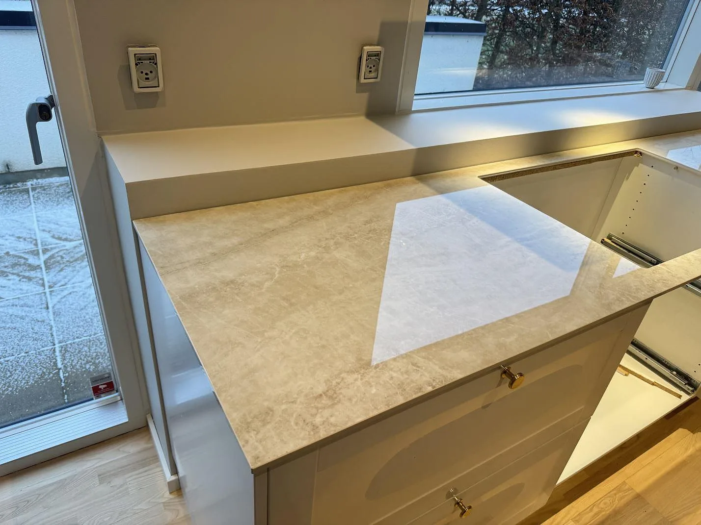 Köksbänkskiva i beige keramik Nuovo Corso Taj Mahal som vänder runt ett hörn med fönsterbänk och balkongdörr i ett kök i Aalborg.
