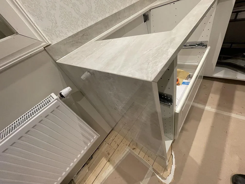 Hörnsektion av köksbänkskiva i Nuovo Corso Taj Mahal keramik med radiator och stommar under montering i ett kök i Skänninge.