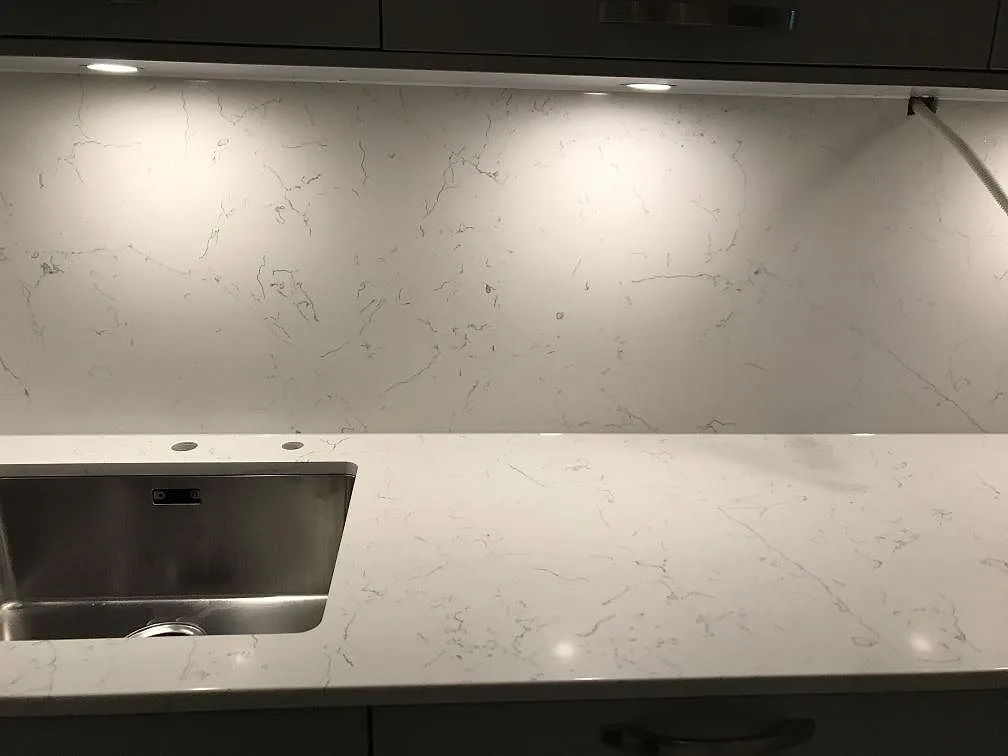 Köksbänkskiva i Quarella Bianco Saturno med underlimmad rostfri diskho och uppvikt stänkskydd i ett kök i Genarp.