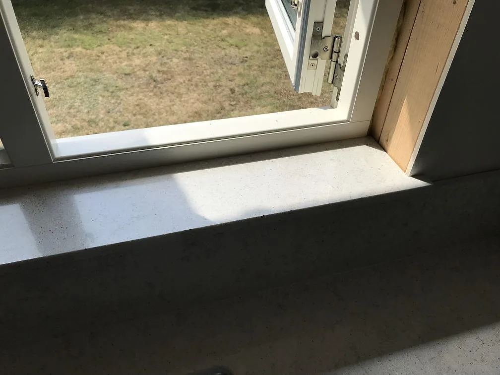 Stenklädd fönsterbänk i vit Quarella Bianco Savoia komposit vid ett öppningsbart fönster i ett kök i Beddingestrand.