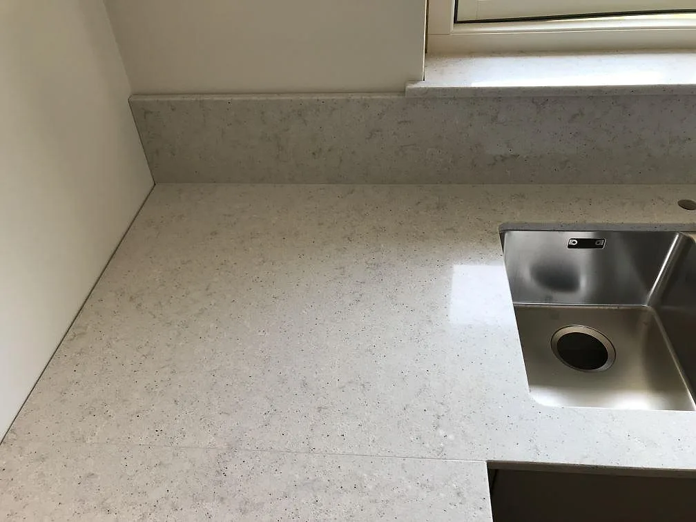 Hörn av köksbänkskiva i Quarella Bianco Savoia komposit med uppvikt stänkkant och rostfri diskho i Beddingestrand.