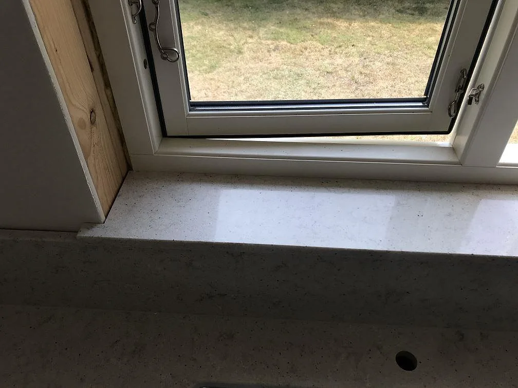Fönsterbänk och bänkskiva i polerad Quarella Bianco Savoia komposit i ett kök i Beddingestrand.