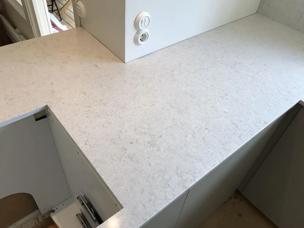 Köksbänkskiva och halvö i ljus Quarella Bianco Savoia komposit med eluttag i ett kök i Beddingestrand, polerad yta.